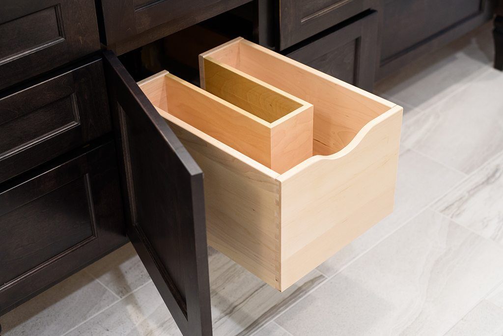 A wooden drawer with two dividers in it is open in a kitchen.