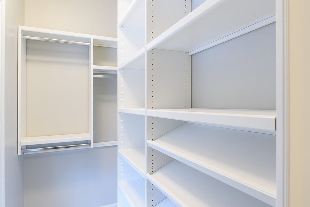 An empty walk in closet with white shelves and a hanging rack.