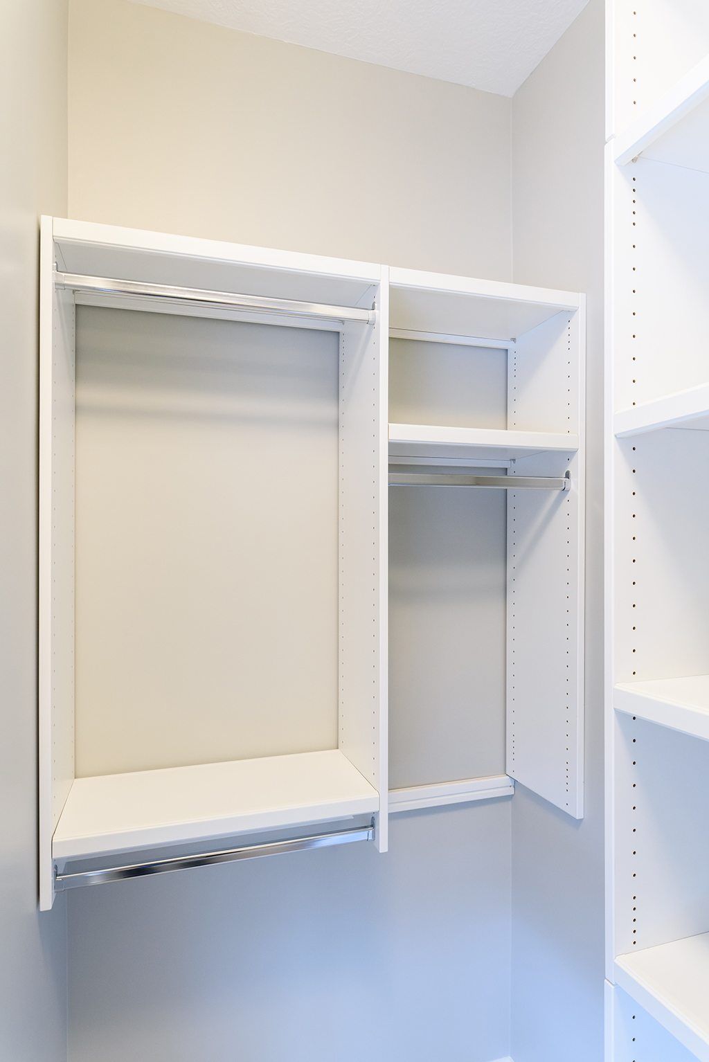 An empty walk in closet with white shelves and clothes racks.