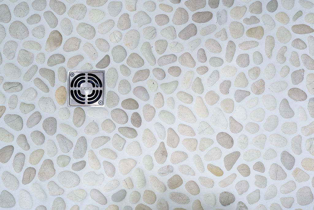 A shower floor with white rocks and a drain.