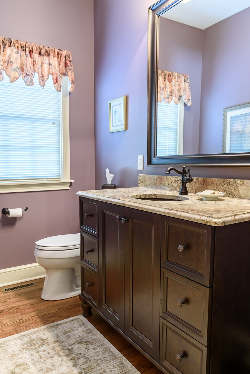 A bathroom with purple walls , a toilet , sink and mirror.