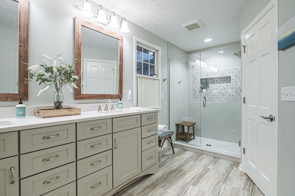 A bathroom with two sinks , two mirrors and a walk in shower.