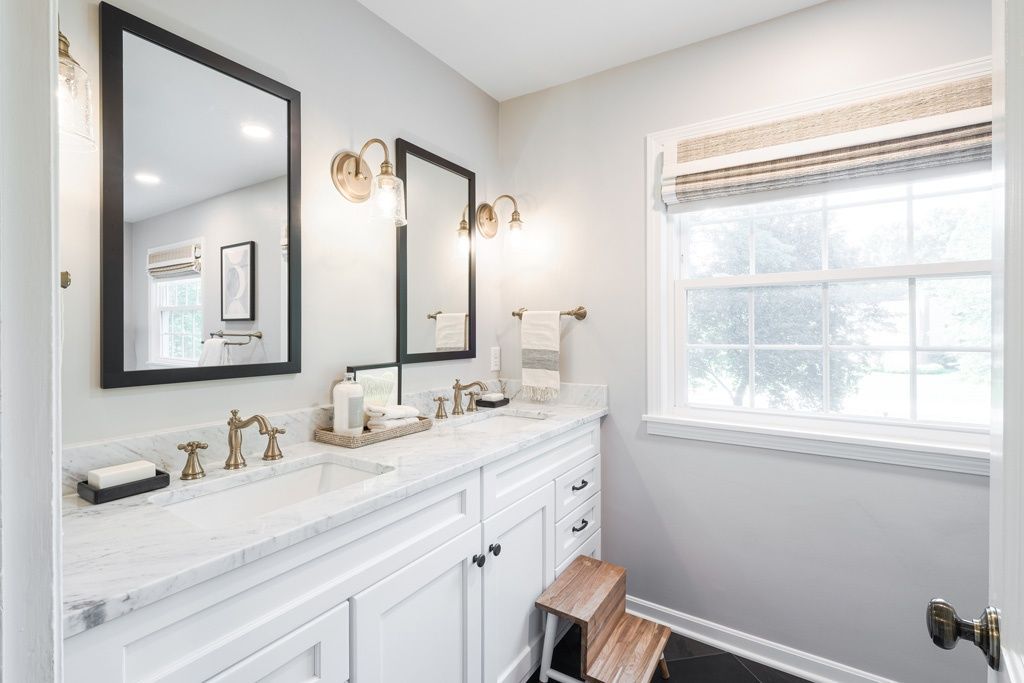 A bathroom with two sinks , two mirrors and a window.