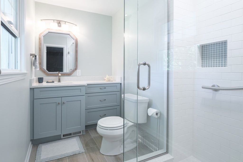 A bathroom with a toilet , sink , mirror and walk in shower.