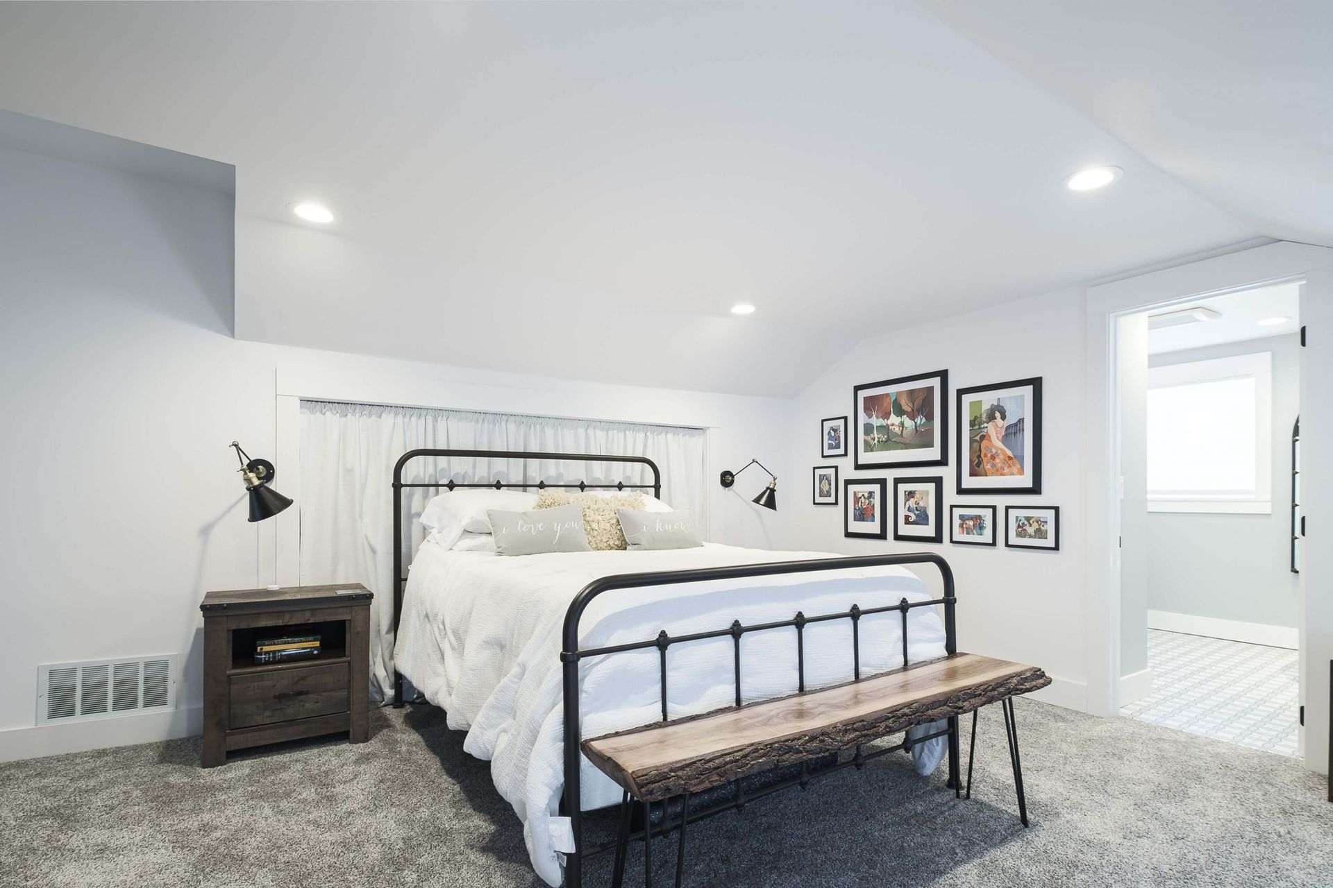 A bedroom with a bed , nightstand , bench and pictures on the wall.