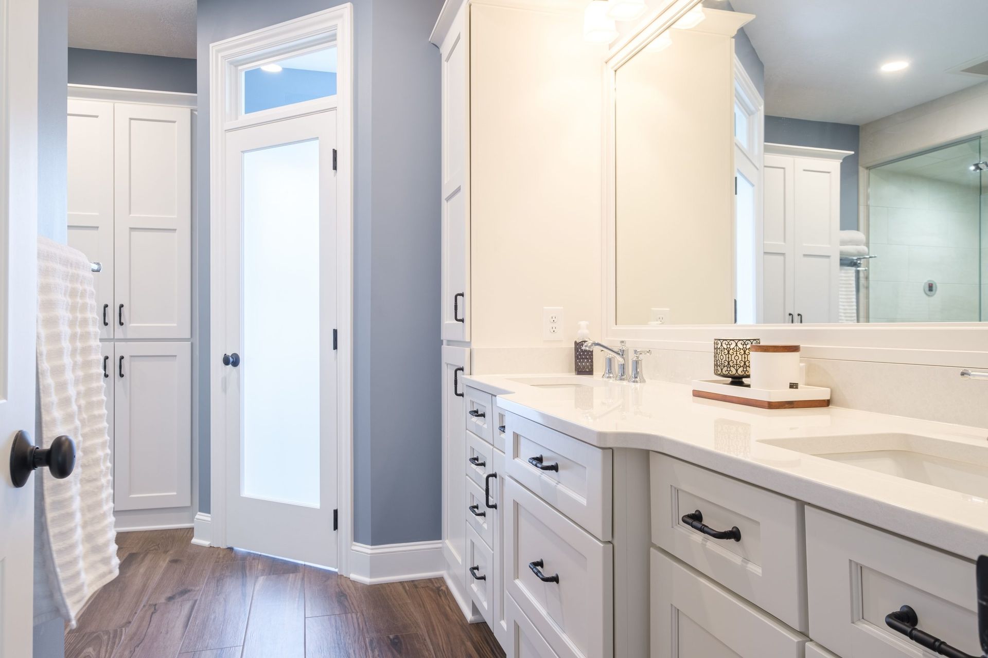 A bathroom with white cabinets , a sink , a mirror and a walk in shower.