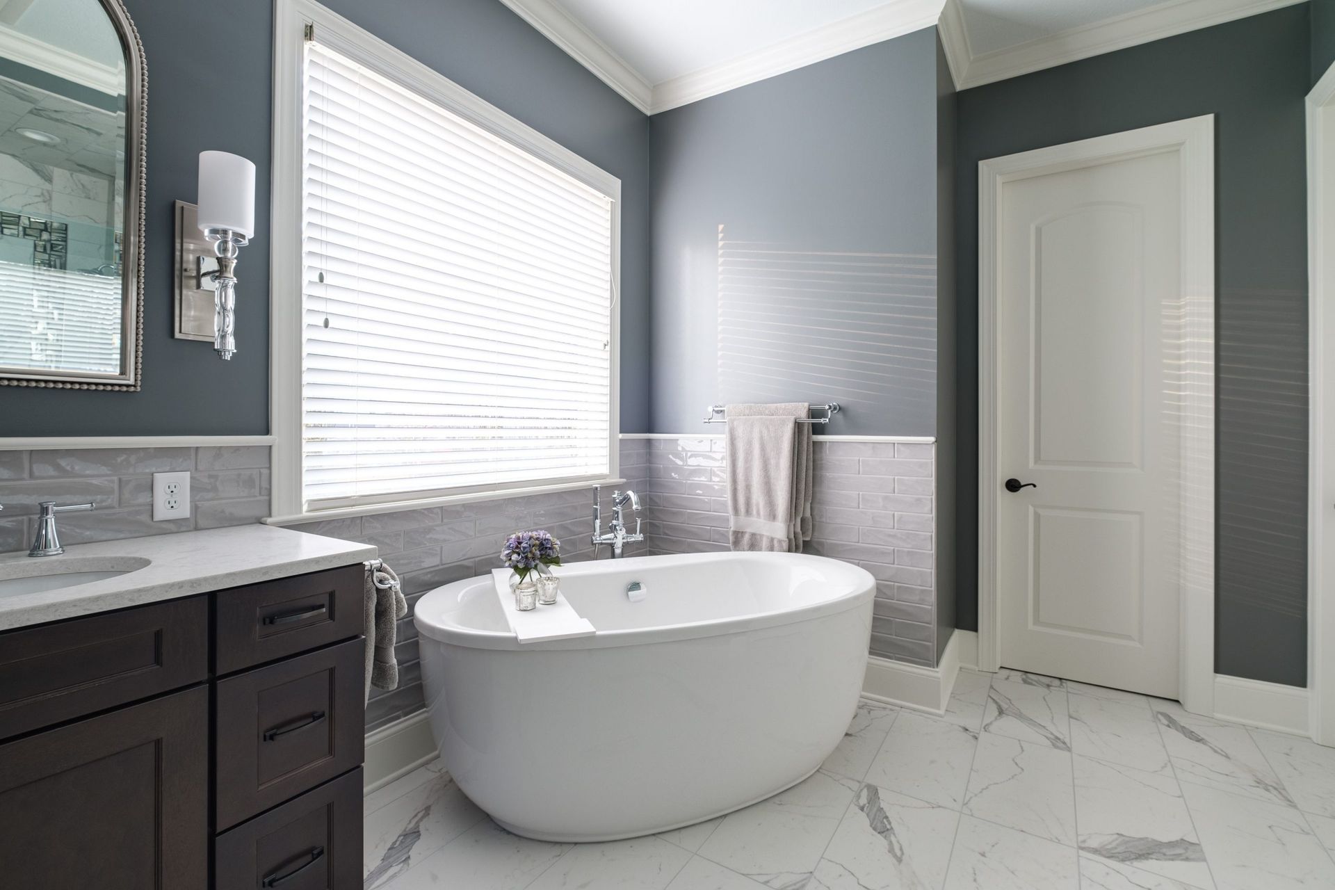 A bathroom with a tub , sink , mirror and window.