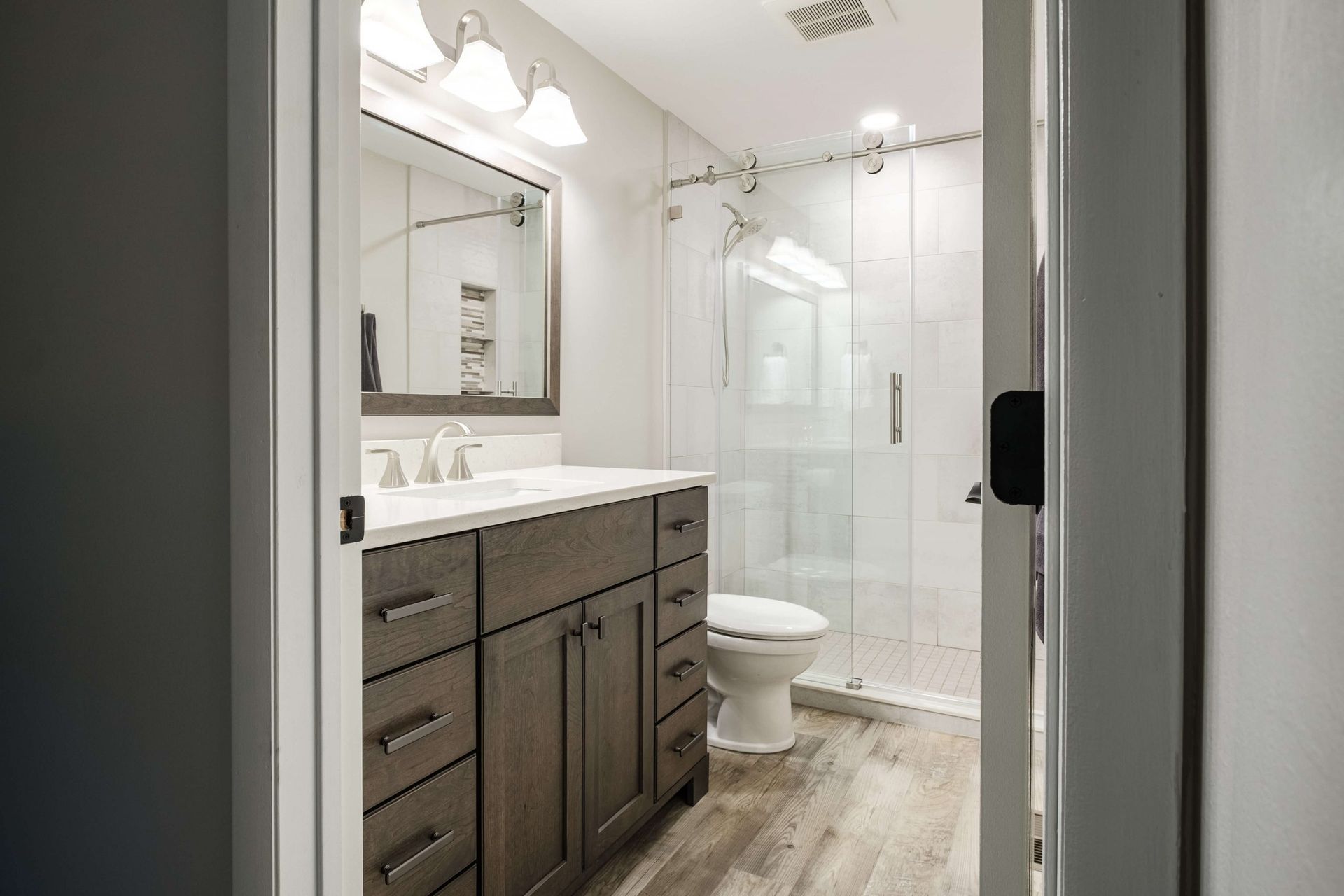 A bathroom with a sink , toilet , mirror and walk in shower.