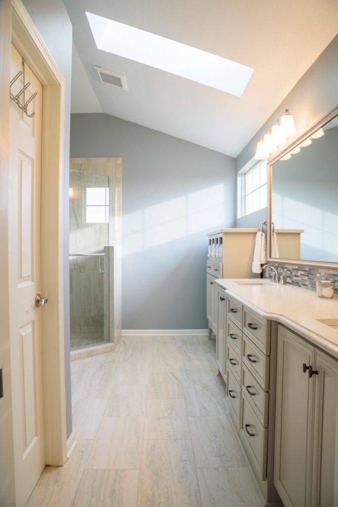 A bathroom with two sinks , a mirror and a skylight.