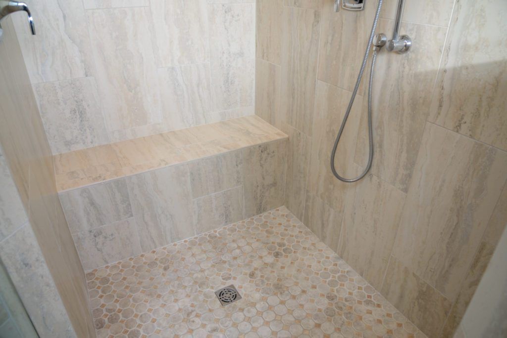 A walk in shower with a bench and a shower head.