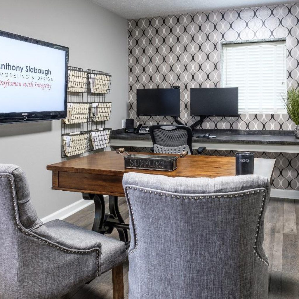A conference room with a table , chairs , computer monitors and a large flat screen tv.