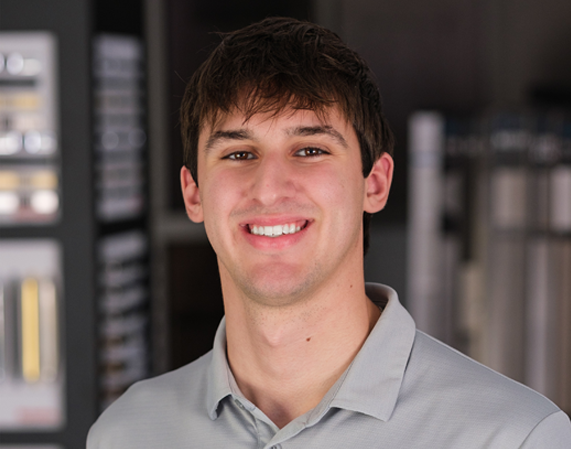 A young man in a grey shirt is smiling for the camera.