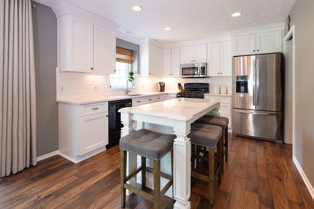 A kitchen with white cabinets , stainless steel appliances , hardwood floors and a large island.