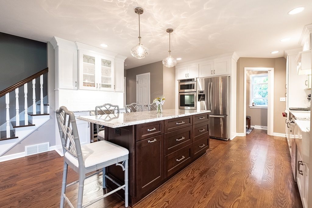 A kitchen with a large island , stainless steel appliances , hardwood floors and white cabinets.