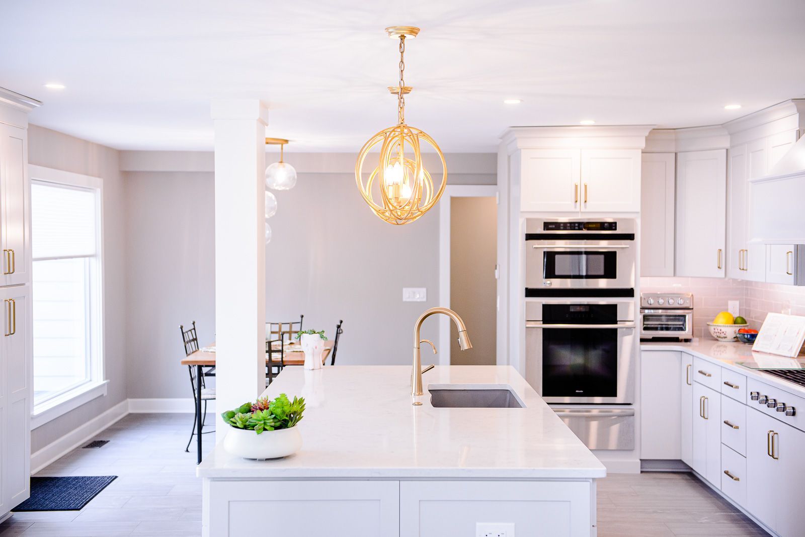A kitchen with white cabinets , stainless steel appliances , a sink , and a large island.