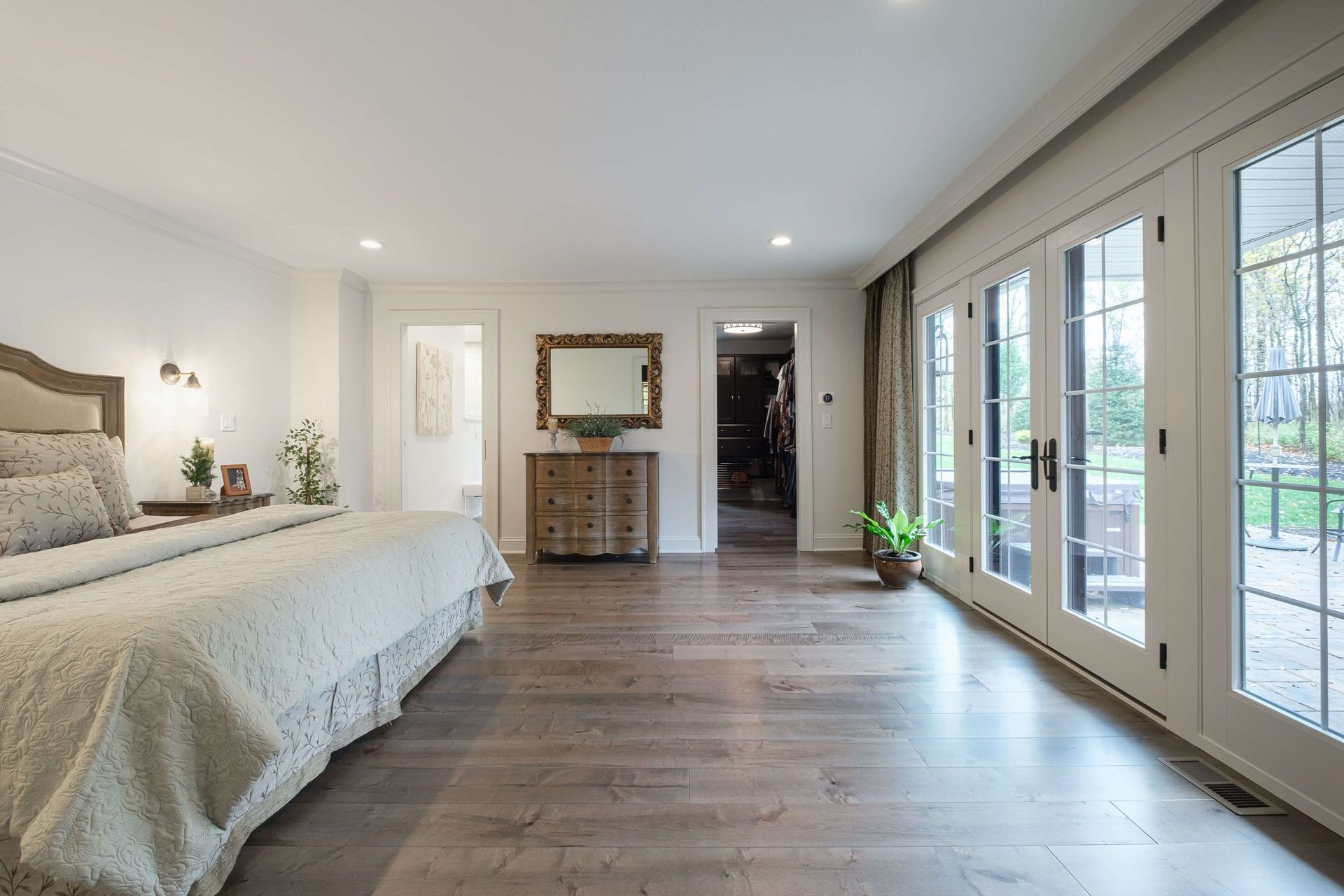 A bedroom with a bed , dresser , mirror and lots of windows.