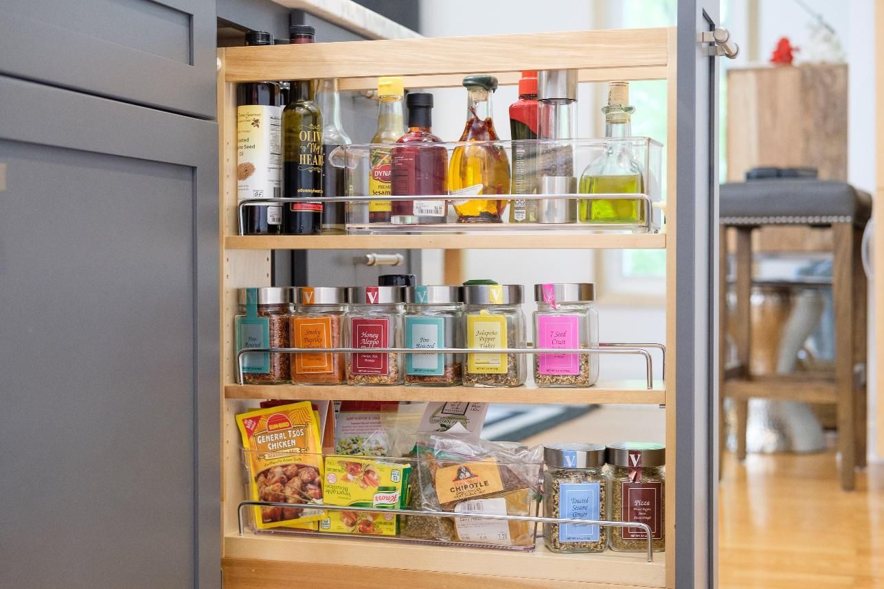 A kitchen cabinet with a pull out spice rack filled with bottles and jars.