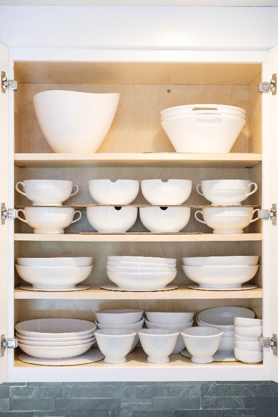 A cabinet filled with white bowls , cups , and plates.