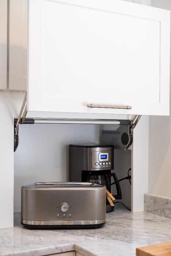 A toaster and coffee maker are under a cabinet in a kitchen.