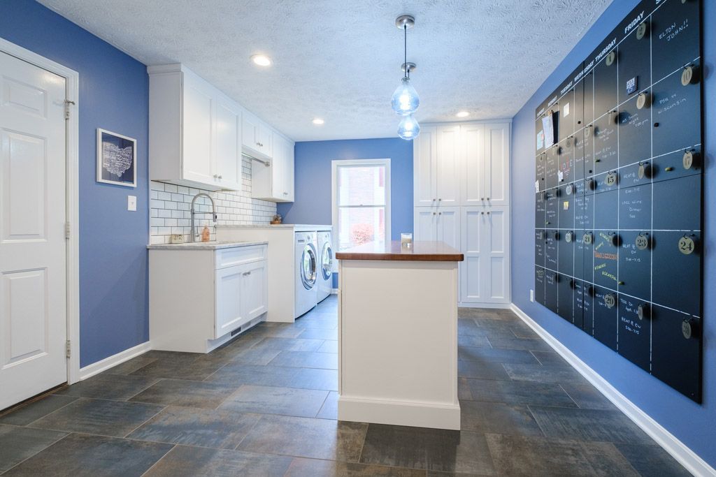 A laundry room with blue walls and white cabinets and a blackboard on the wall.