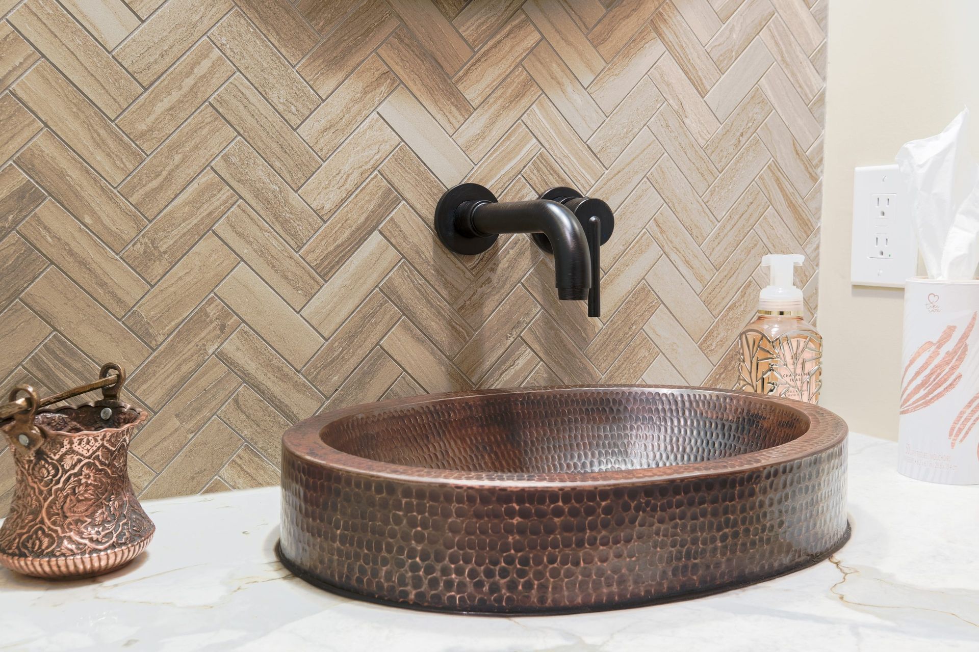 A bathroom with a copper sink and a herringbone tile wall.