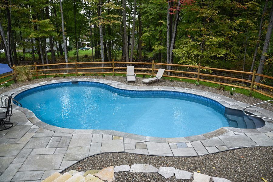 A large swimming pool is surrounded by a wooden fence and chairs.