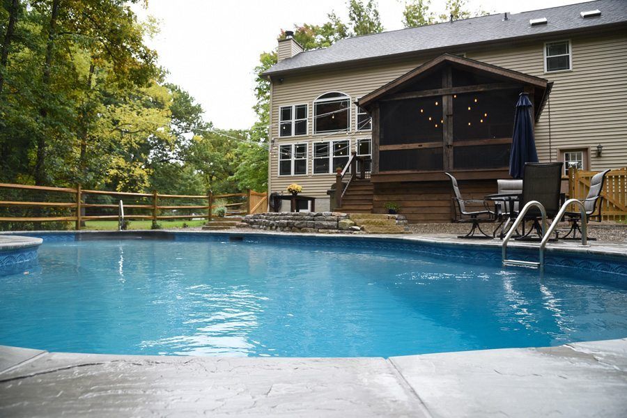 A large swimming pool in front of a house with a screened in porch