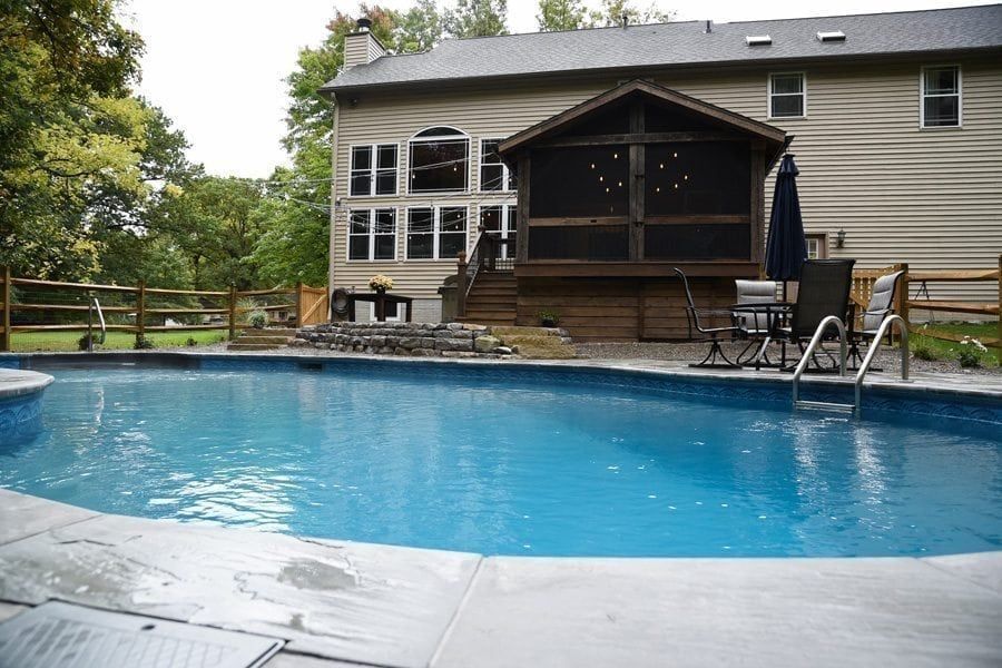 A large swimming pool in front of a house with a screened in porch