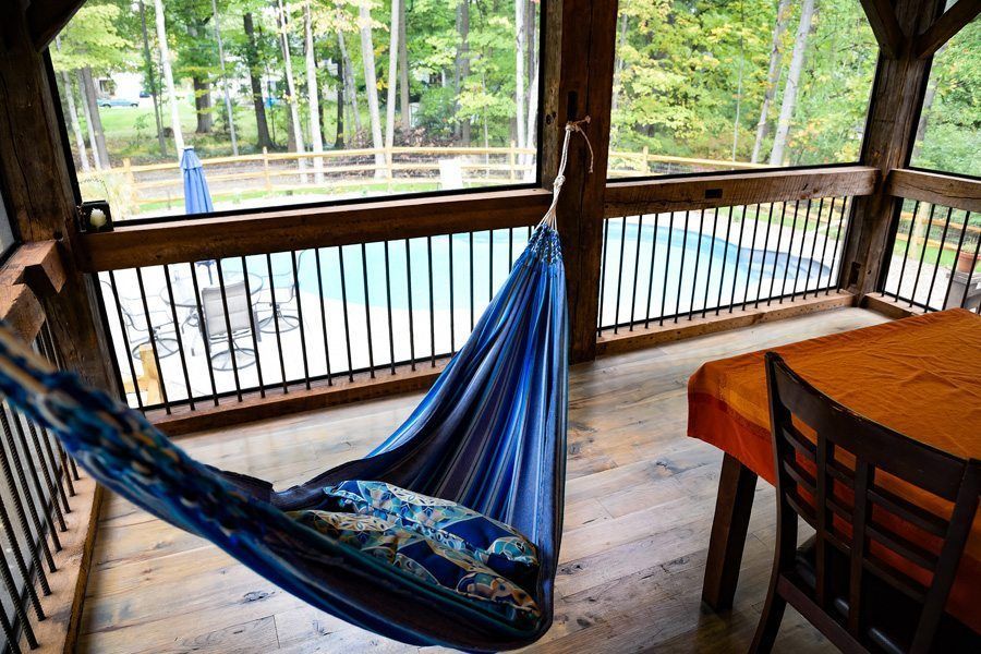A blue hammock is hanging on a screened in porch next to a table and chairs.
