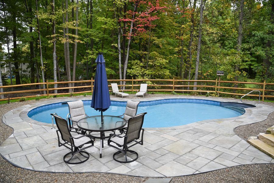 A swimming pool with a table and chairs and an umbrella surrounded by trees.