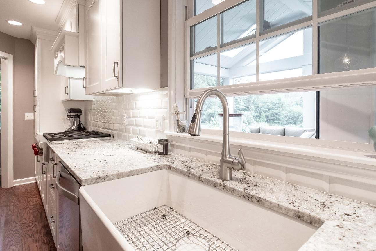 A kitchen with white cabinets , granite counter tops , a sink and a window.