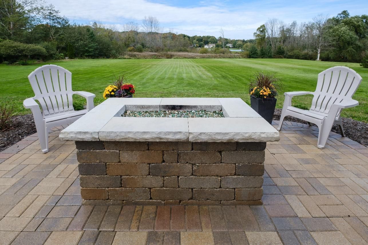 A fire pit is sitting on a brick patio next to two chairs.