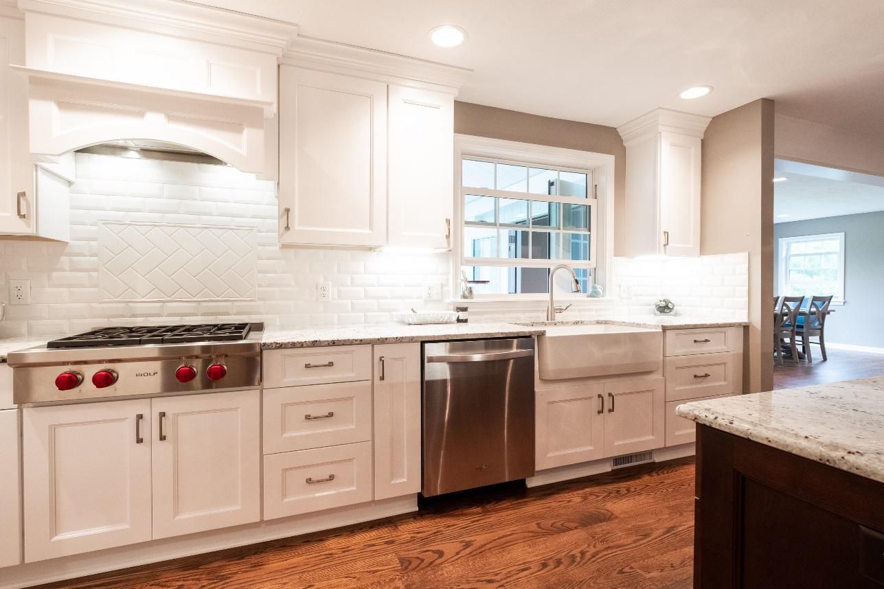 A kitchen with white cabinets , a stove , a sink , and a stainless steel dishwasher.