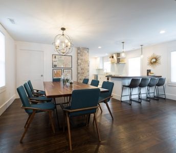 A dining room with a table and chairs and a kitchen in the background.