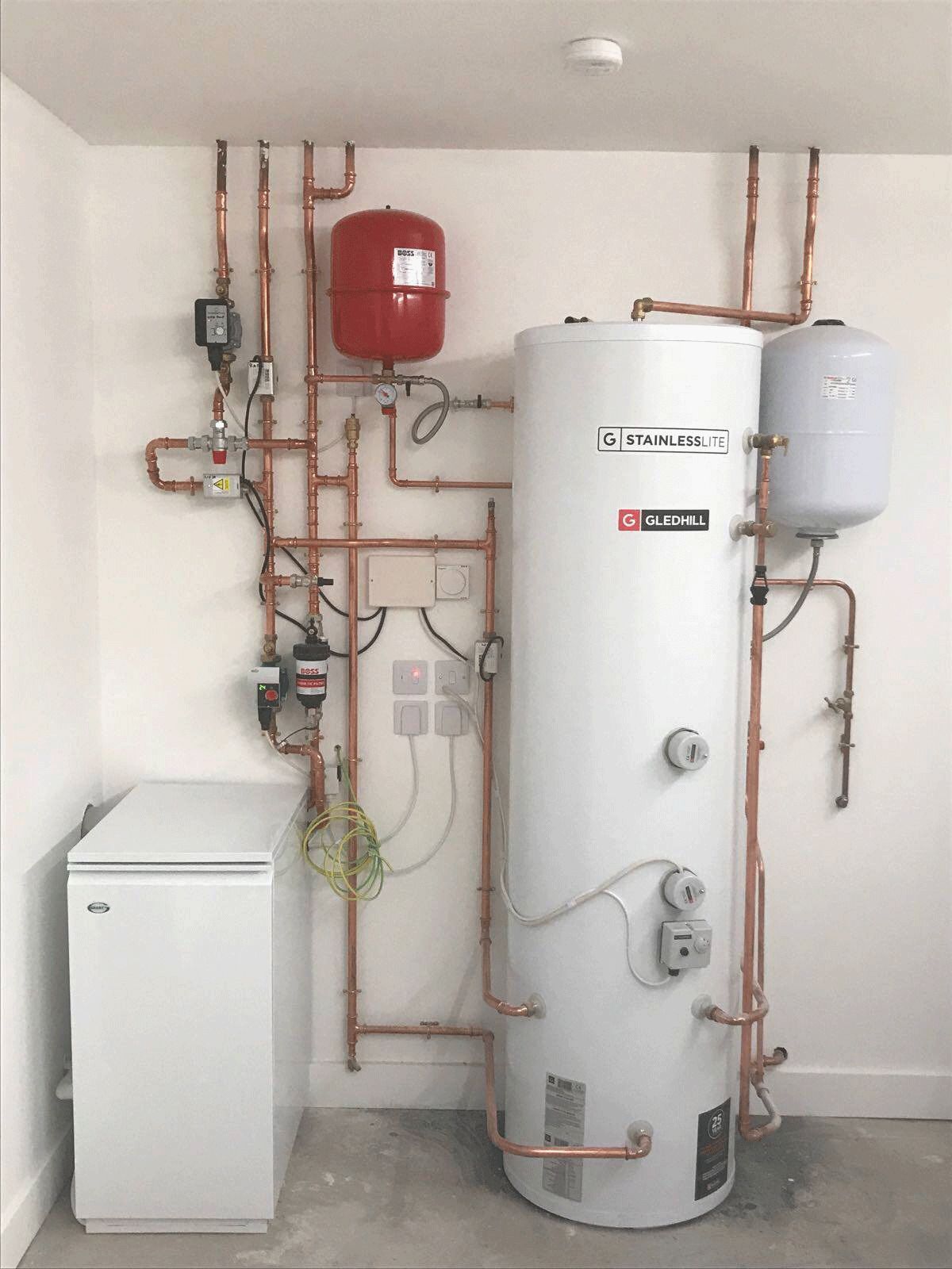 A white water heater is sitting in a room with copper pipes.
