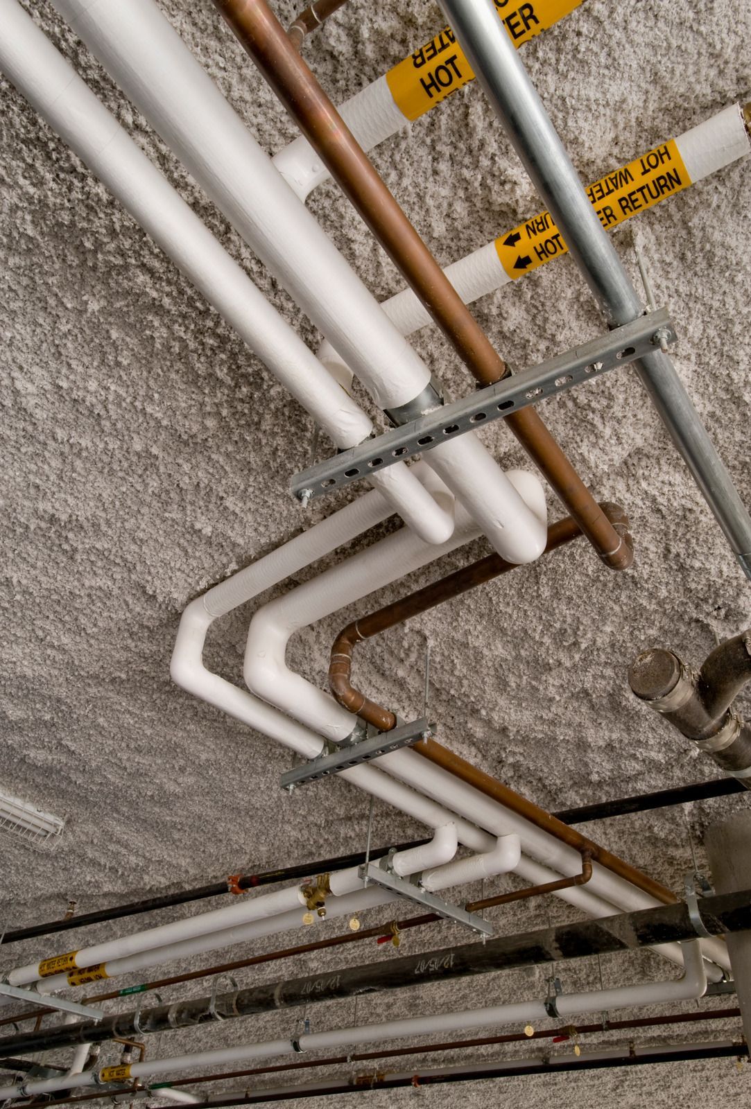 A bunch of pipes are hanging from the ceiling and one of them says hot