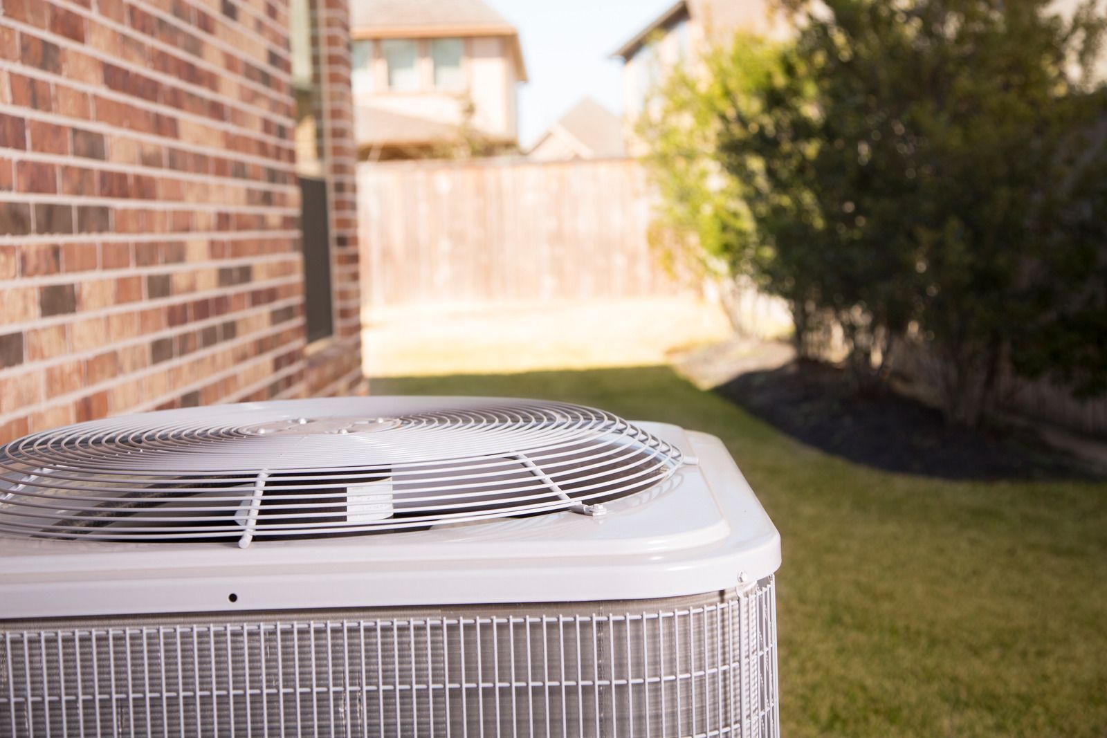 An air conditioner is sitting in the backyard of a brick house.