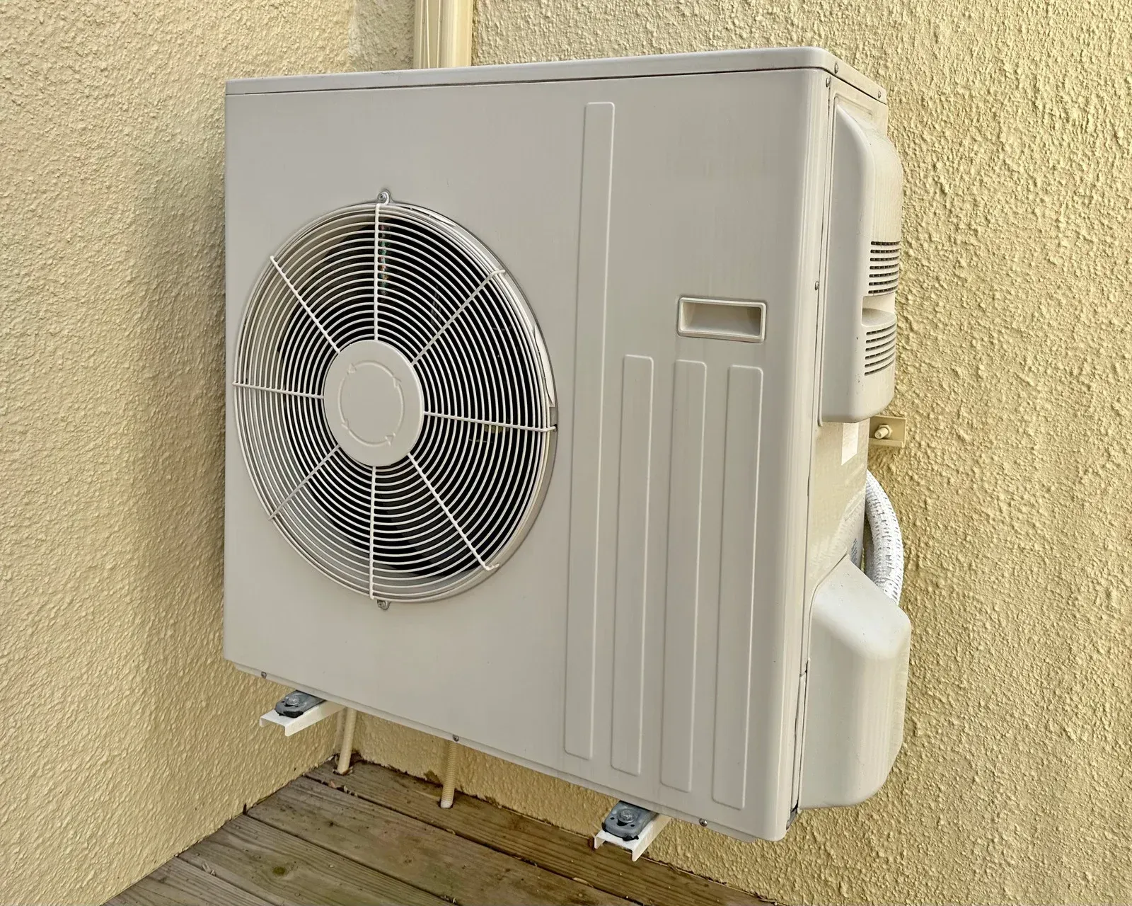 A white air conditioner is mounted to the side of a building.