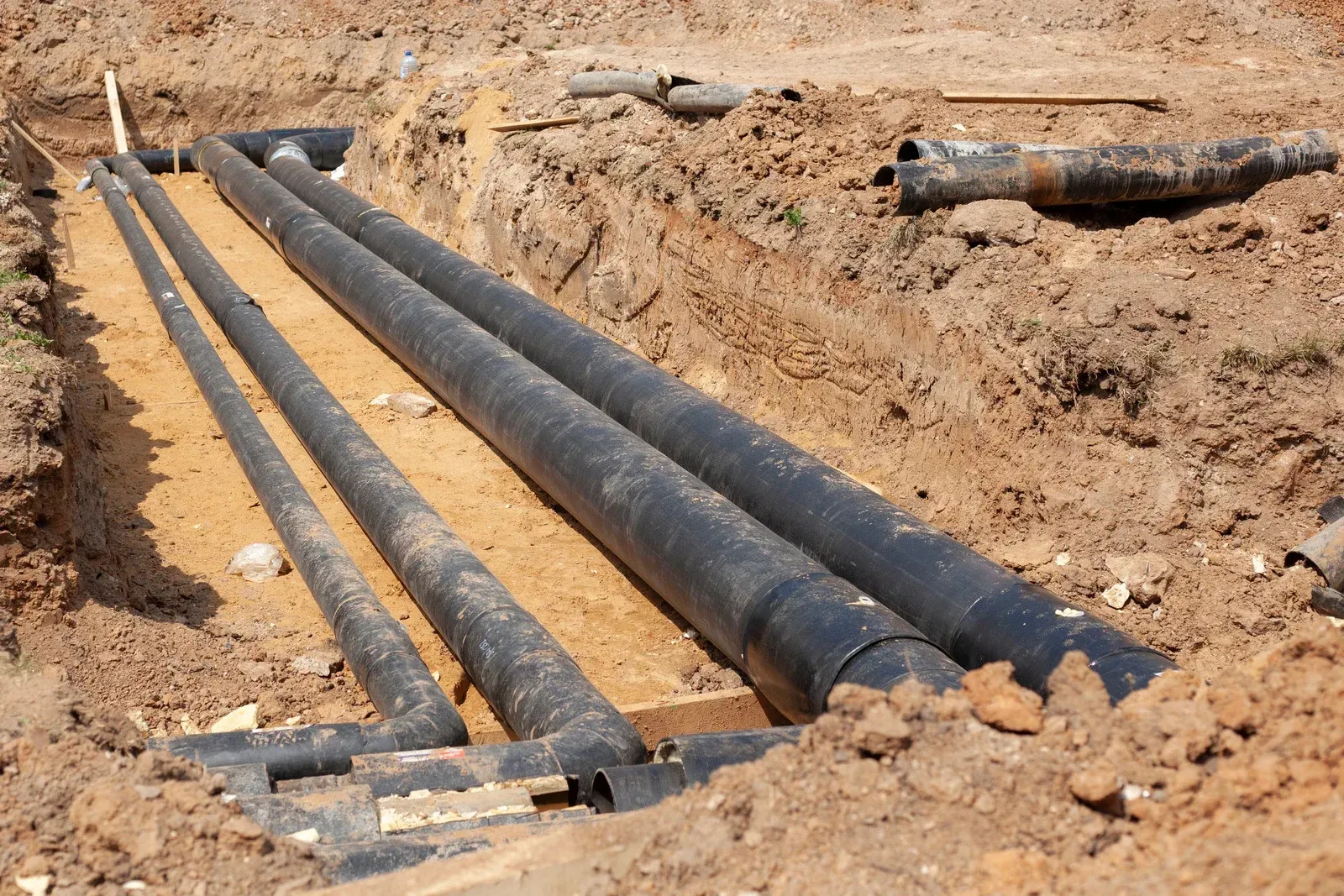A black pipe is being installed in a trench of dirt.