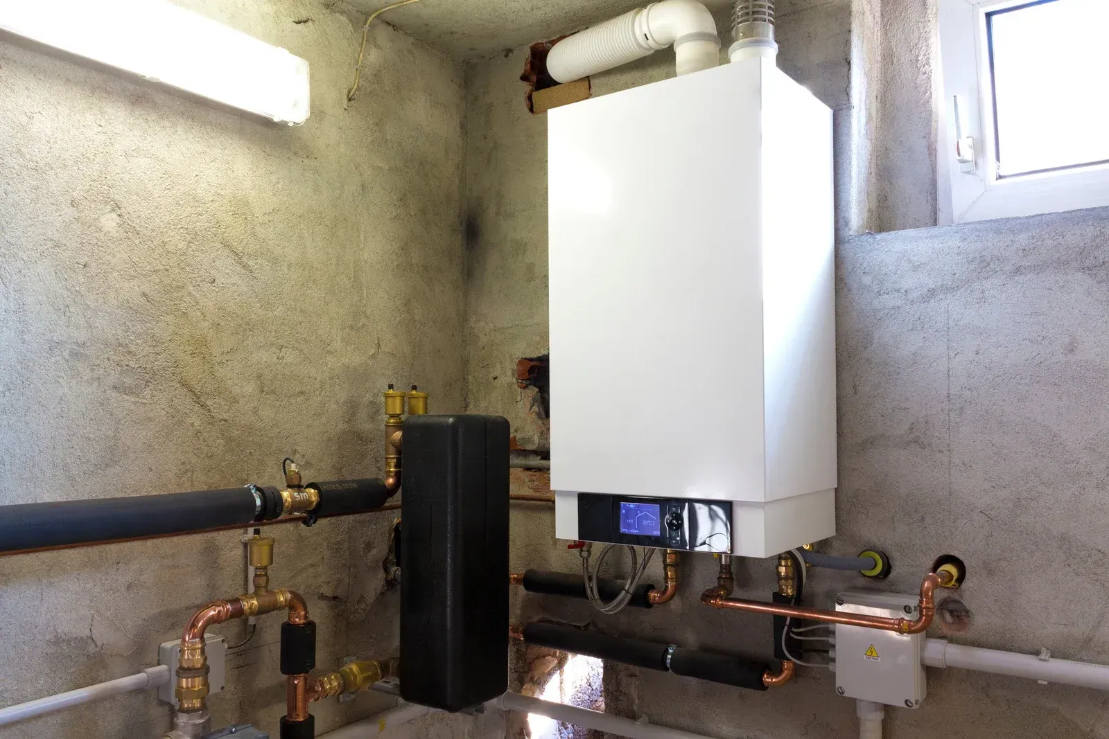 A white boiler is sitting in a room next to a window.