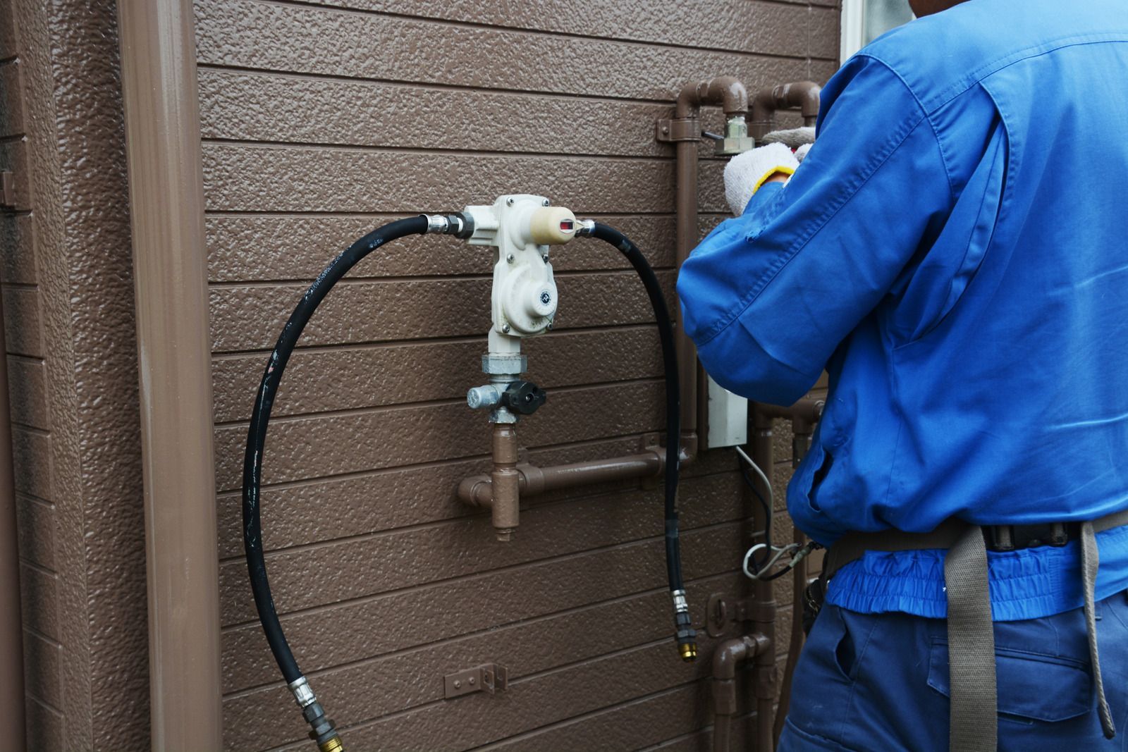 A man in a blue shirt is working on a pipe outside of a building.