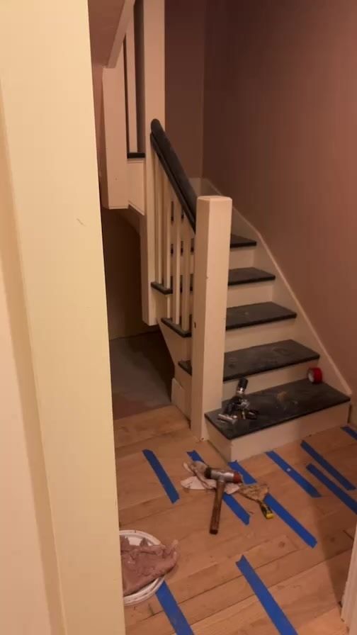 A staircase is being painted in a room with blue tape on the floor