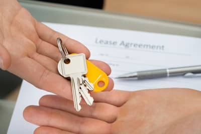 Close-up of a person giving keys to a man with a Rental Agreement in the background