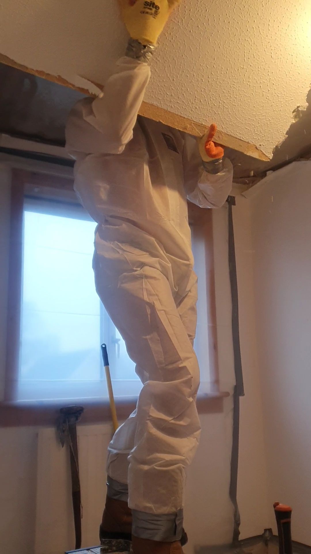 a person in a white suit is spraying a ceiling with a spray bottle .