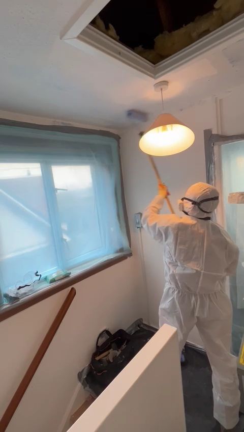 a man in a protective suit is cleaning a light fixture in a room .