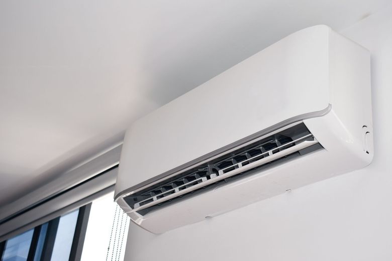 White wall-mounted air conditioning unit on a white wall near a window.