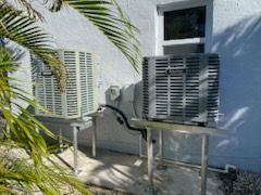 Two outdoor air conditioning units mounted on metal stands against a white building.
