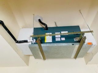 An overhead air conditioning unit installed in a ceiling, with ductwork and support brackets.