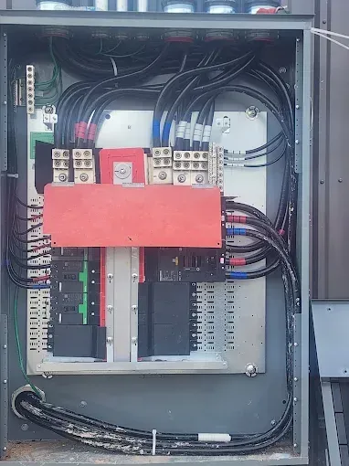 Open electrical control panel with wiring, terminals, and a red cover inside a metal cabinet