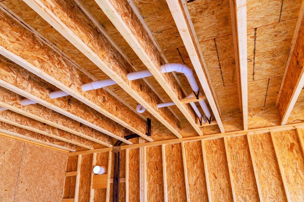 Exposed wooden ceiling framing with white pipes and wiring in an unfinished room